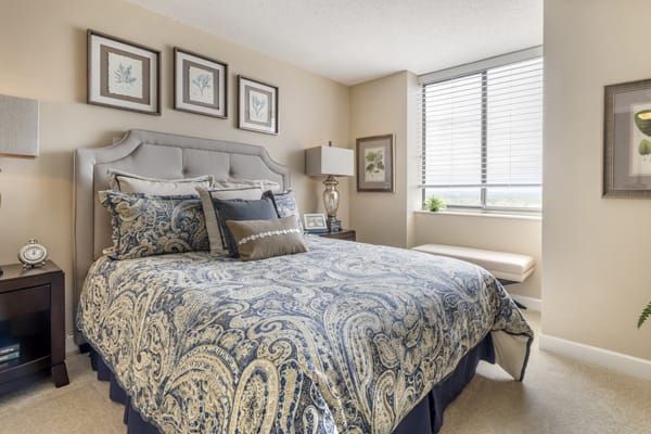 A well-decorated bedroom featuring a patterned bedspread, artwork on the walls, and natural light from a large window.