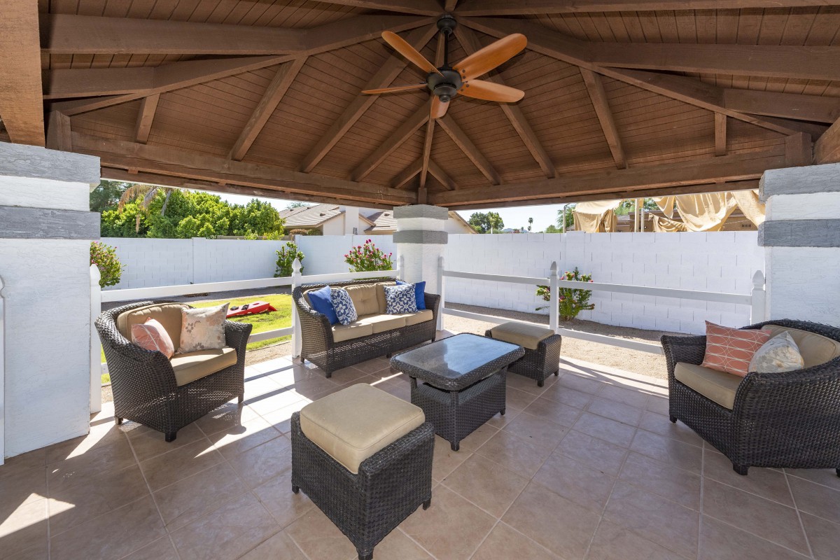 A cozy outdoor patio area with a gazebo, featuring wicker furniture and a ceiling fan, perfect for relaxation in a garden setting.