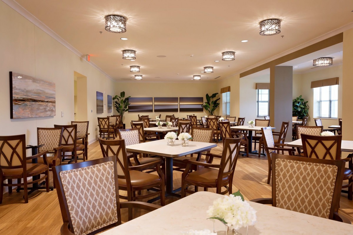 A spacious dining room with elegantly arranged tables and chairs, featuring modern lighting fixtures.