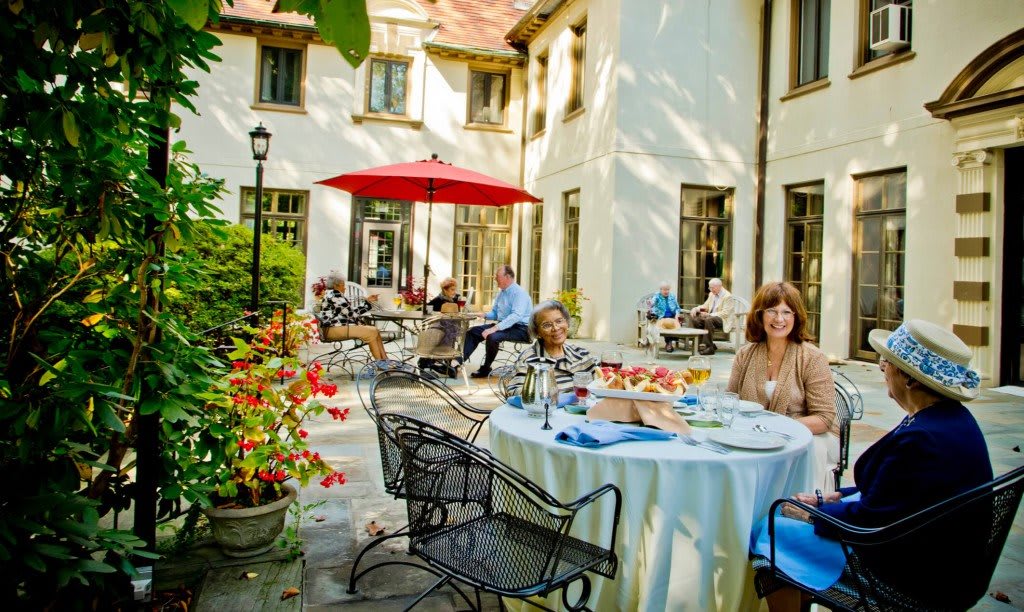 A group of people enjoying a meal on a sunny outdoor patio with a garden view.