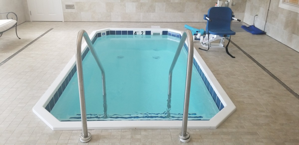 An indoor swimming pool with a metal ladder and an accessibility chair on the side.