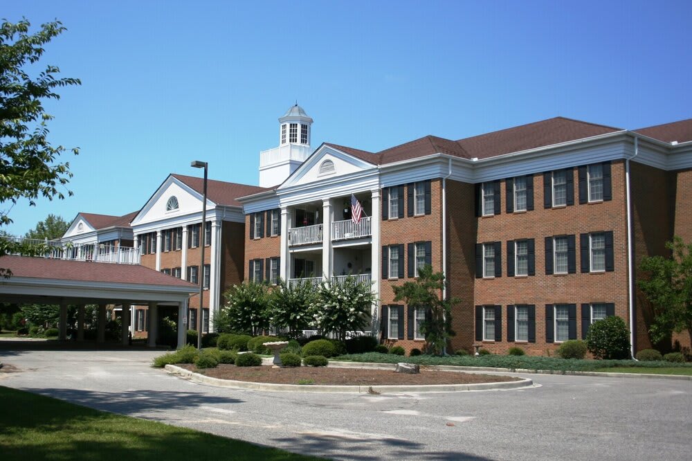 A colonial-style red brick building with a landscaped entrance and clear blue sky.