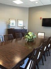 A conference room with a large wooden table and chairs, adorned with a floral centerpiece.