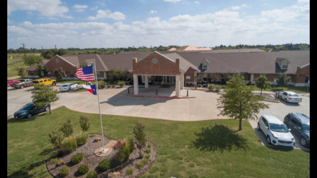 A large building with an entrance driveway, surrounded by greenery and featuring flags in the foreground.
