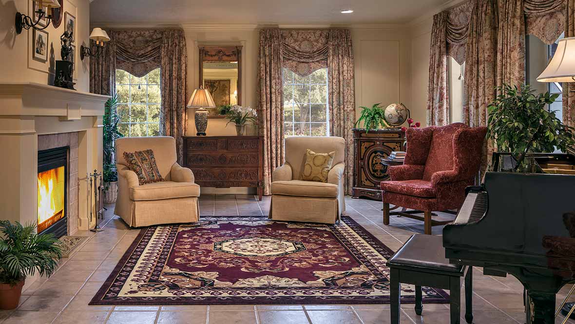 A cozy living room with various chairs and a patterned rug, complemented by elegant curtains and warm lighting.