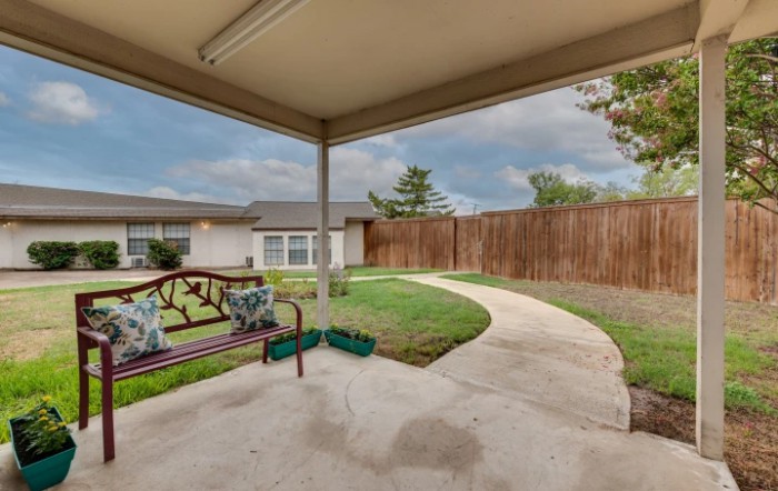 A cozy backyard with a covered patio, featuring outdoor seating and a well-maintained lawn enclosed by a wooden fence.