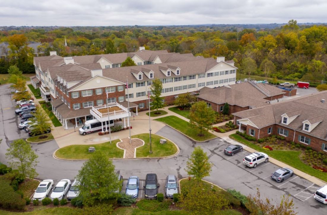 Aerial view of a large residential building surrounded by trees and a parking lot.