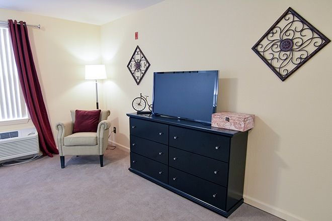 A cozy living room corner with a dresser, TV, lamp, and chair.