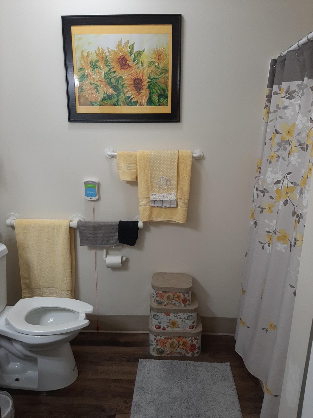 A tidy bathroom with sunflower artwork, coordinating towels, and floral shower curtain.