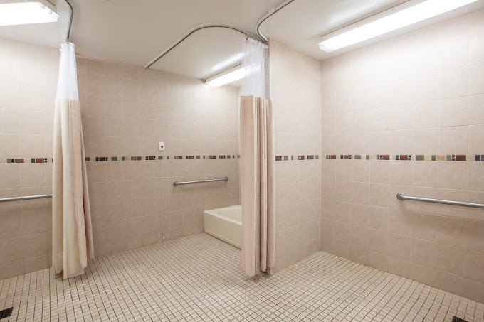 A clean and spacious tiled bathroom featuring shower stalls with curtains and accessible handrails.