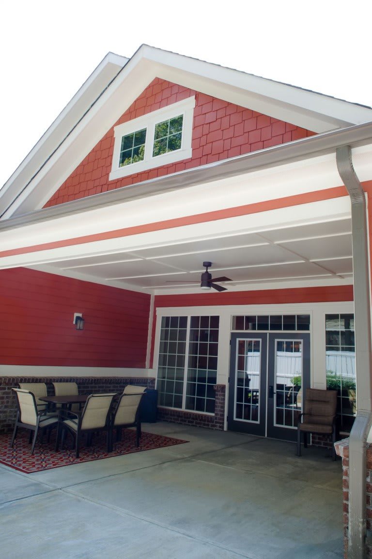 A cozy patio area with outdoor seating and a ceiling fan under a red gable roof.