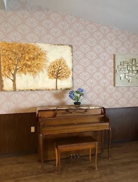 A cozy room featuring a wooden piano decorated with flowers, adorned by vintage wallpaper and artistic wall hangings.