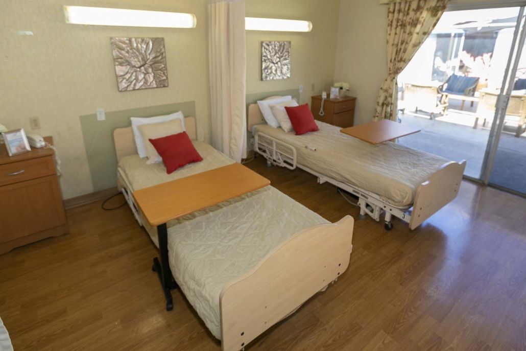 A hospital room with two beds equipped for patient care, featuring wooden floors and privacy curtains.