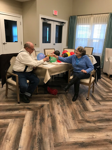 Two elderly individuals enjoying a moment of interaction at a table, surrounded by colorful objects.