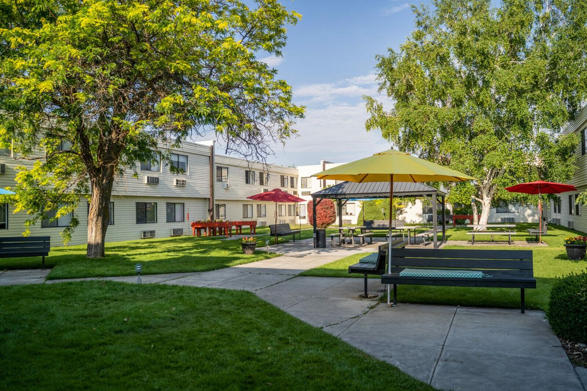 An apartment complex courtyard with benches, umbrellas, and lush greenery.