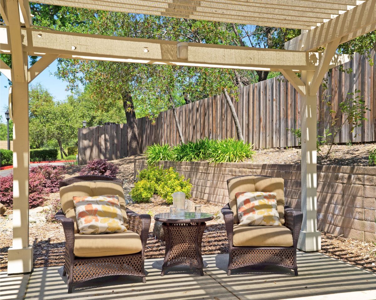 A cozy patio area with wicker chairs under a pergola, surrounded by a lush garden.