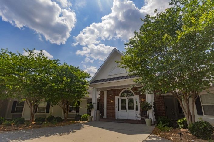 A charming house with a gabled roof, surrounded by lush trees under a partly cloudy sky.