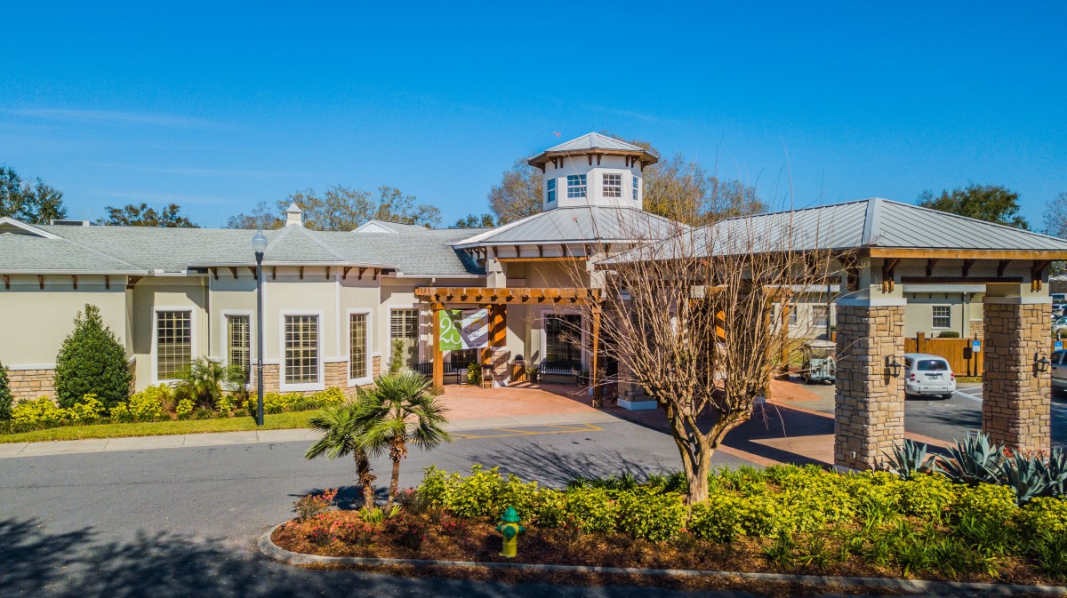 A hotel building with a landscaped entrance featuring palm trees and trimmed bushes under a clear blue sky.