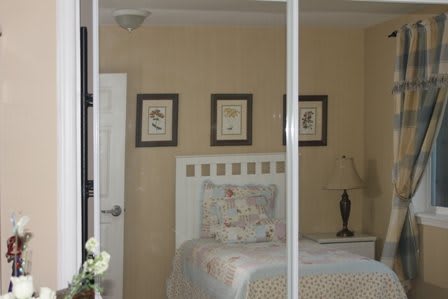 A cozy bedroom with a bed, decorative pillows, and wall art reflected in a mirror.