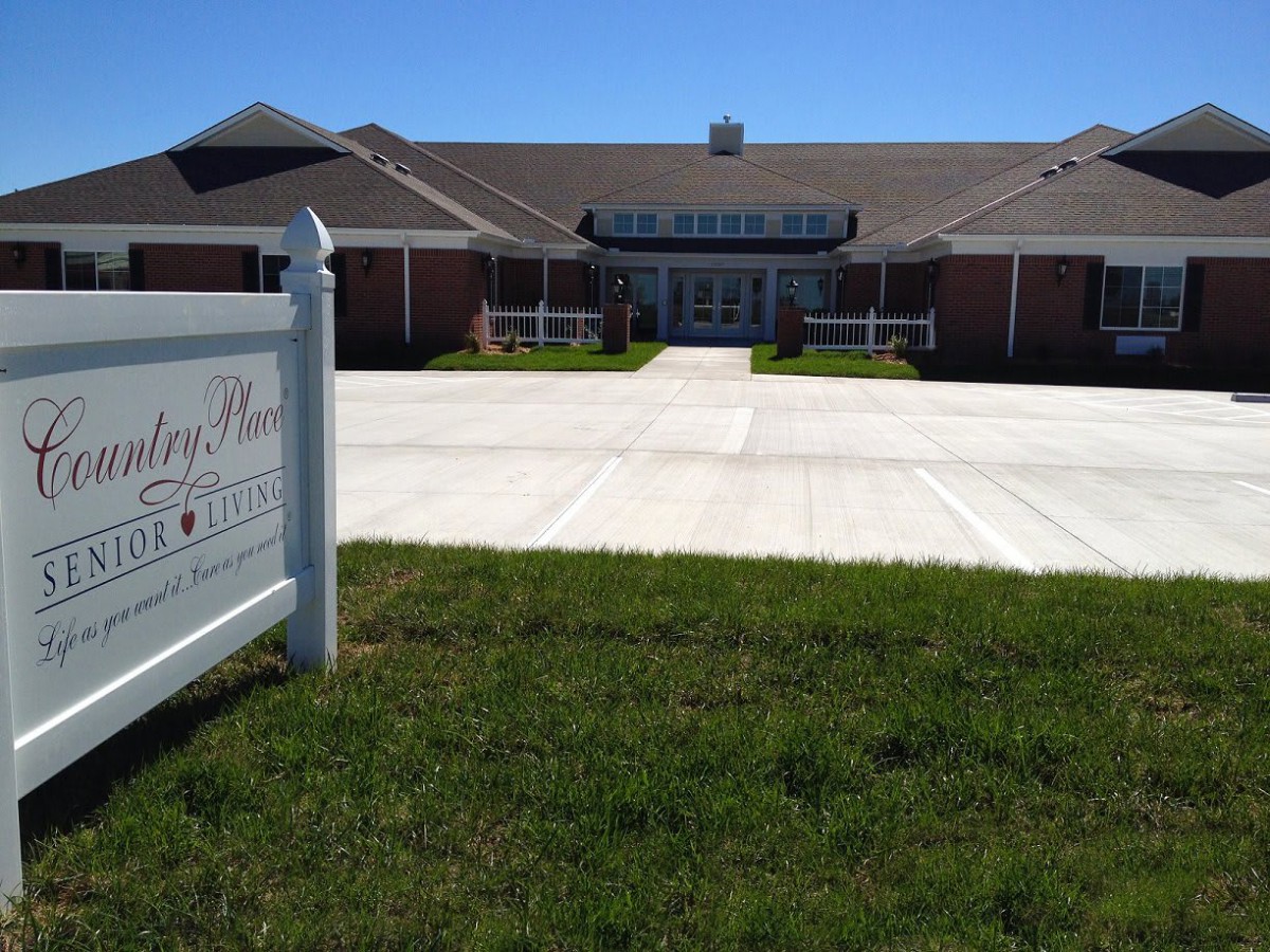 A building with a front lawn and walkway, featuring a sign on the left.