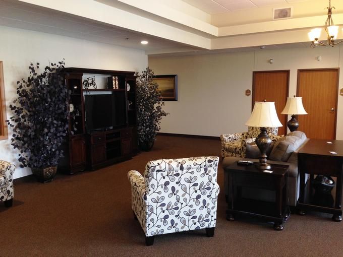 A cozy living room with a patterned chair, sofas, lamps, and a television.
