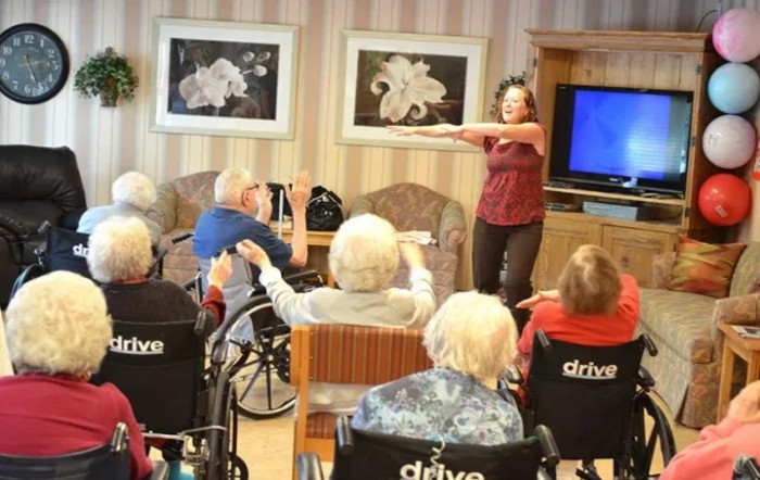 An activity leader guides a group of elderly individuals in an exercise session at a nursing home.