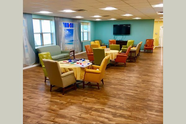 A well-lit meeting room with colorful chairs and tables, featuring a television and large windows.