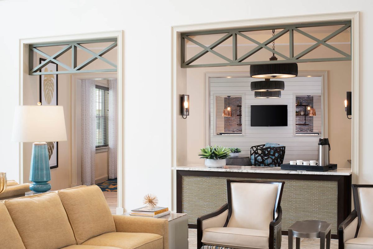A modern living room with neutral tones featuring a sofa, armchair, and a TV in the background.