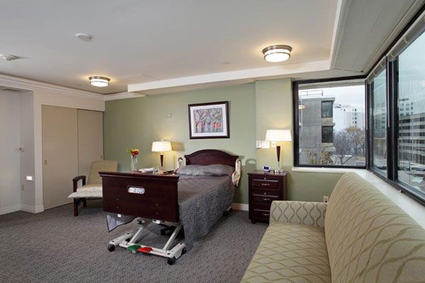 A well-furnished hospital room with a medical bed, chairs, and lamps.