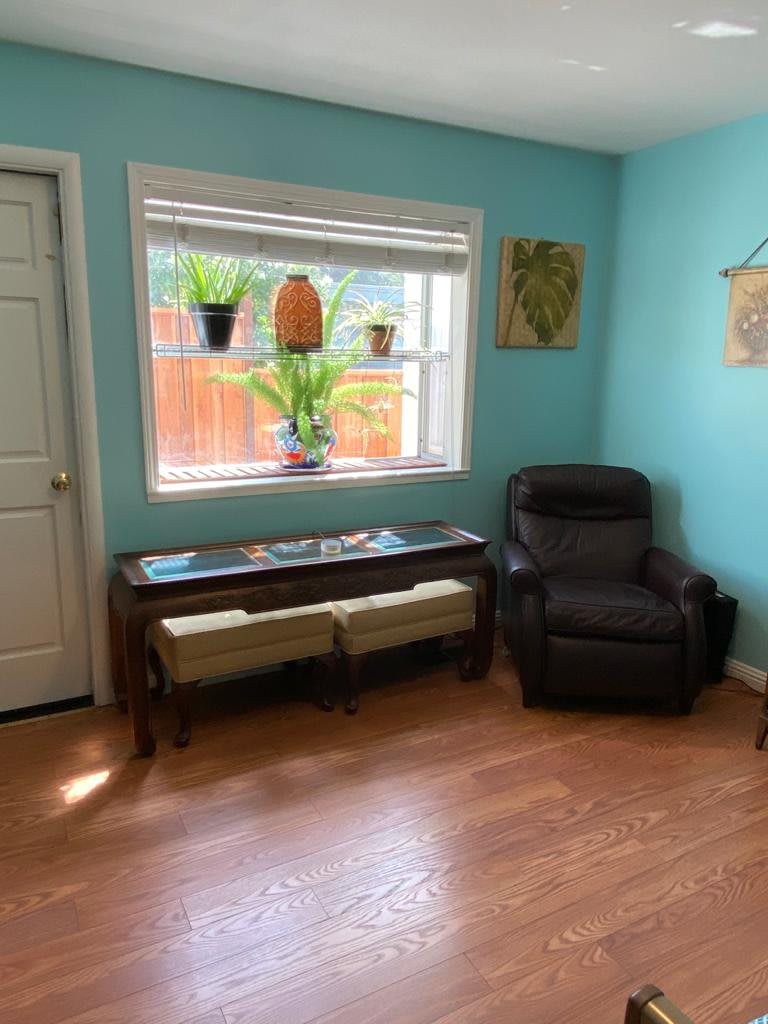 A cozy living room with a leather armchair, a console table beneath a window adorned with potted plants.