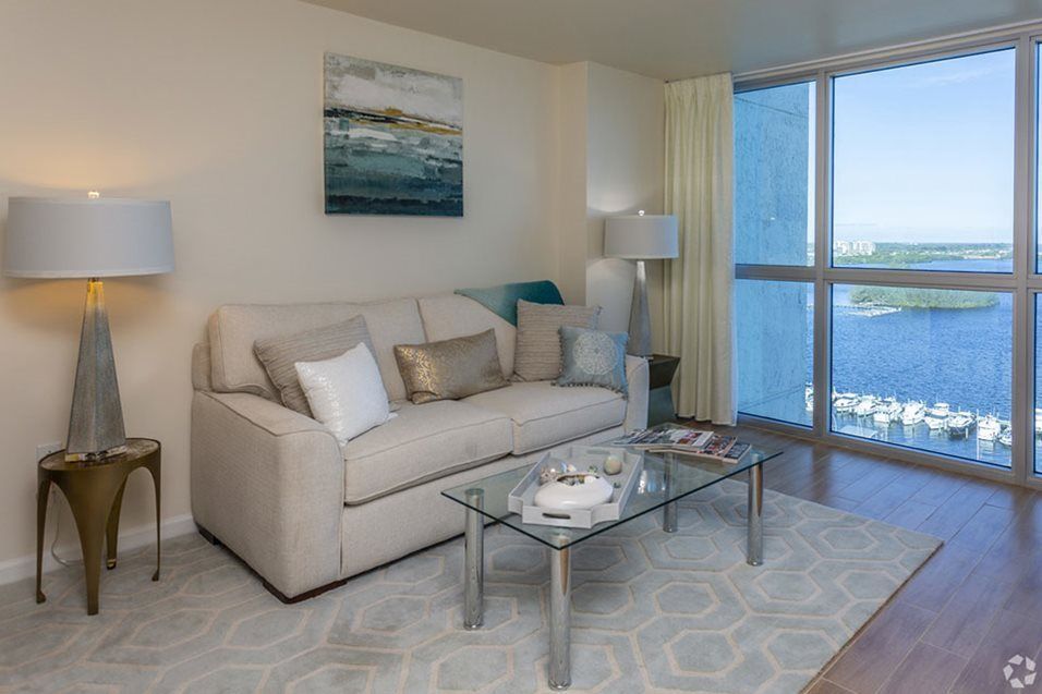 A cozy living room featuring a comfortable sofa, glass coffee table, and large window with curtains.
