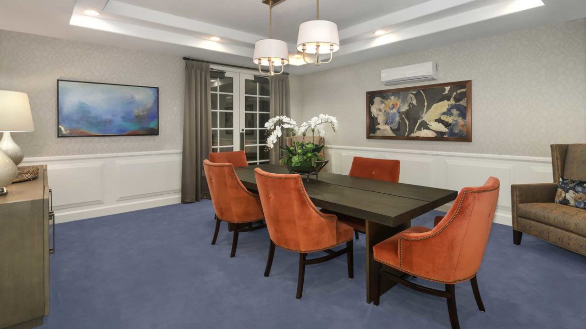 A modern dining room with orange chairs and a dark wood table, accented by a chandelier and artwork on the walls.