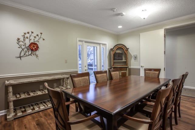 A well-furnished dining room with a large wooden table and chairs, featuring elegant decor and a cabinet in the background.