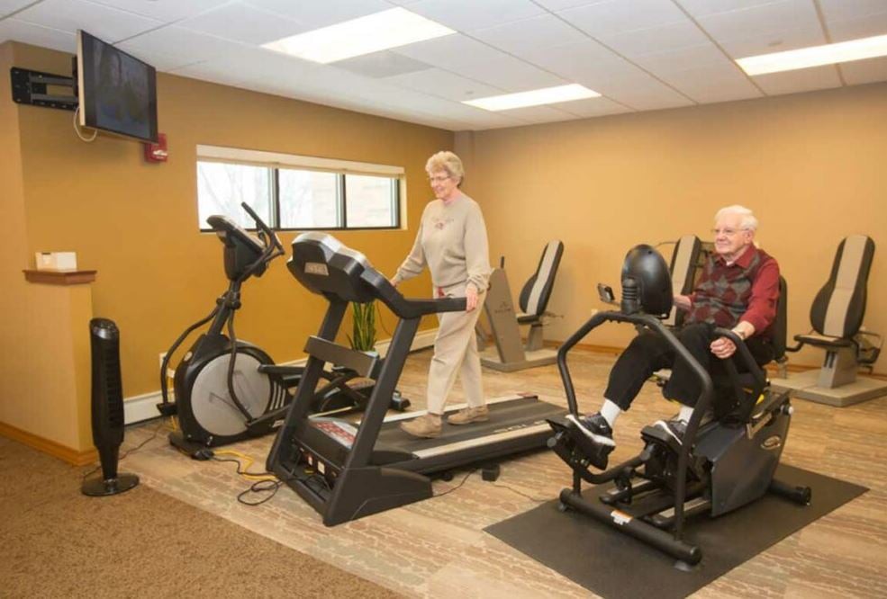 Senior adults exercising in a gym using a treadmill and stationary bike.