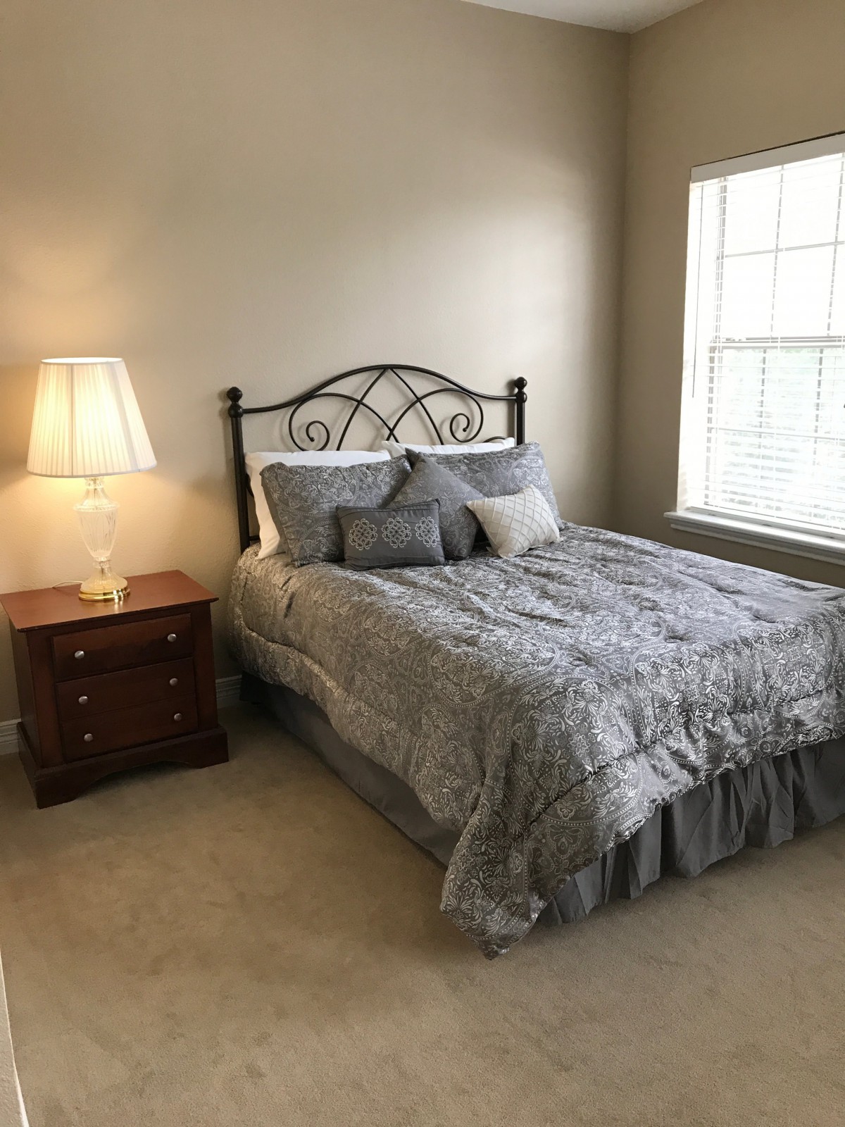 A cozy bedroom with a neatly made bed, a nightstand, and a lamp by the window.