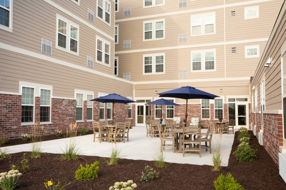A well-furnished patio area with tables, chairs, and umbrellas in front of a multi-story building.