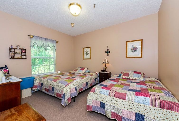 A cozy bedroom with two single beds adorned with colorful quilts, featuring a window that lets in natural light and decorated walls with framed artwork.