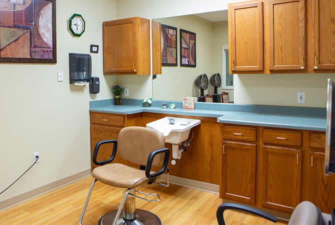 An empty hair salon station with a chair, sink, and wooden cabinets.