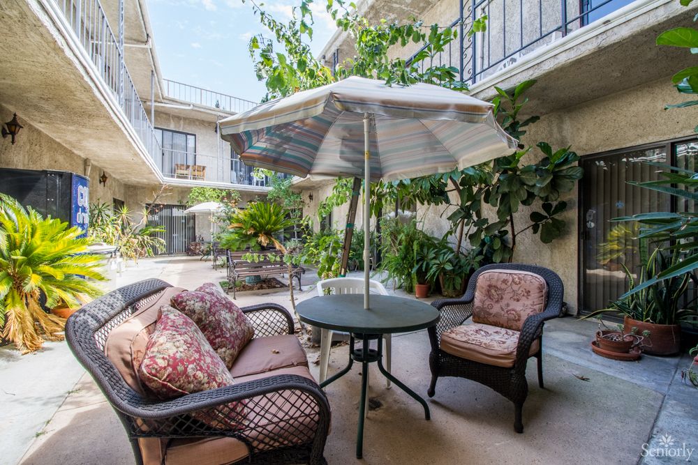 A cozy patio area with cushioned chairs, a round table, and an umbrella surrounded by lush plants.