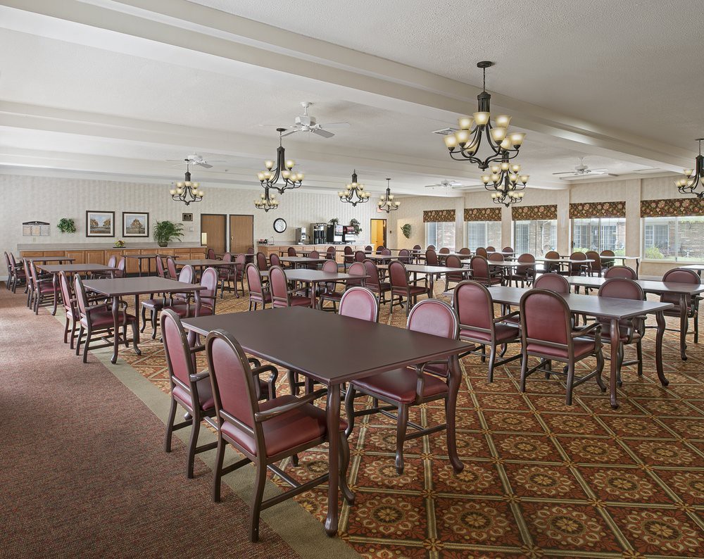 A spacious dining area featuring multiple tables and chairs, ornate chandeliers, and a patterned carpet.