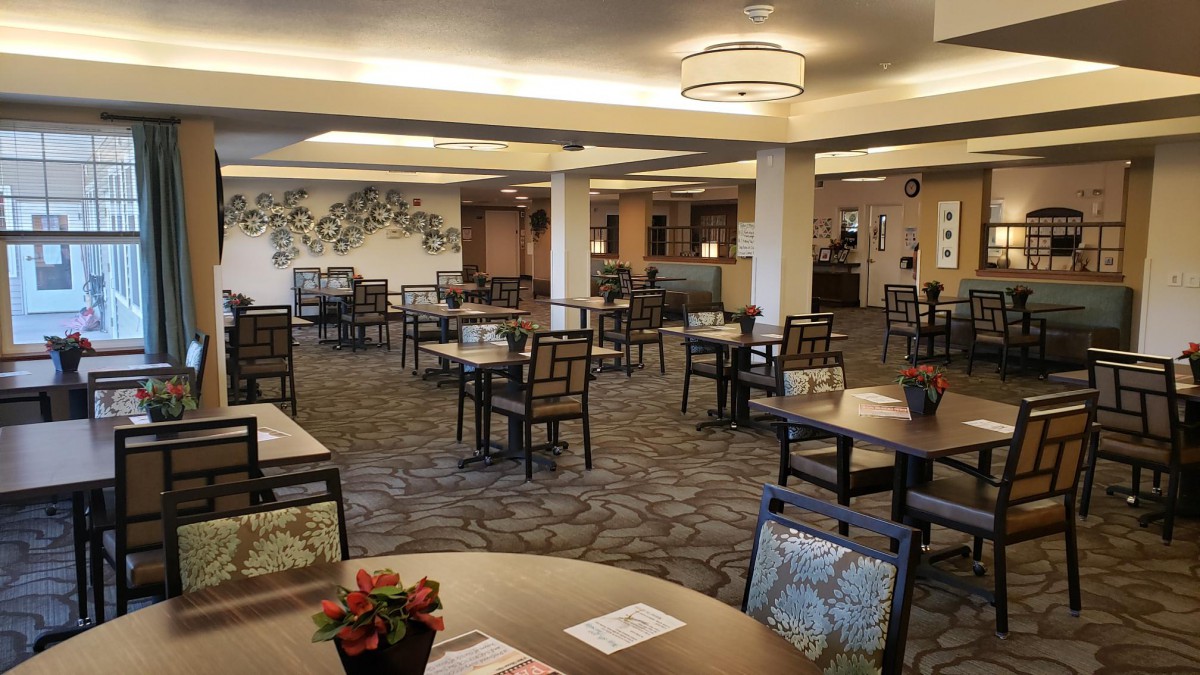 A spacious dining area with neatly arranged tables and chairs, featuring modern lighting and decorative elements on the walls.