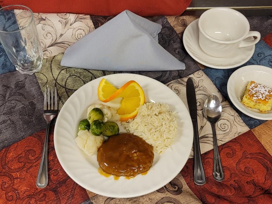 A well-arranged dinner plate featuring rice, gravy-covered meat, brussels sprouts, and a fruit garnish, set on an elegantly laid table.