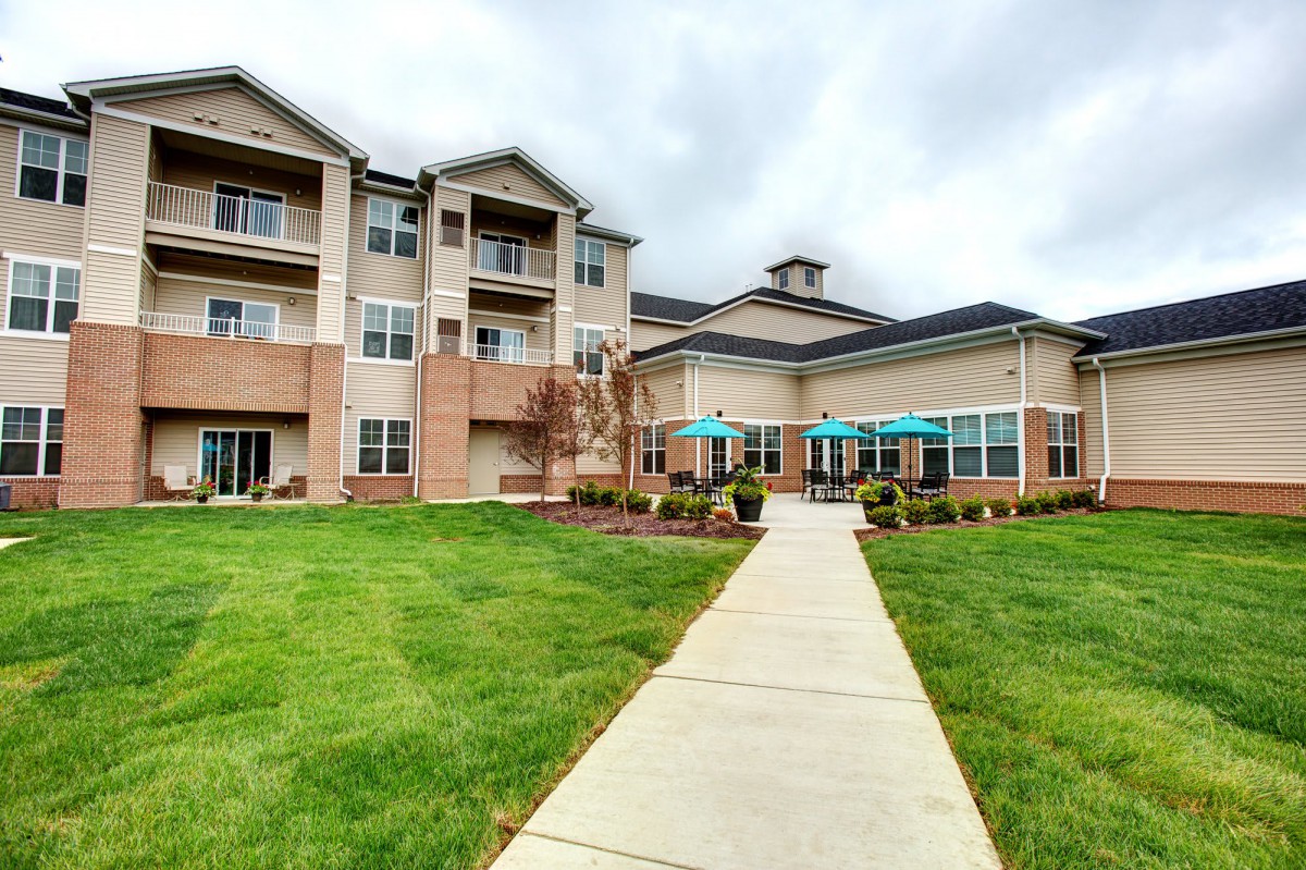 A modern residential apartment building with well-maintained lawns and a clear pathway leading to the entrance.