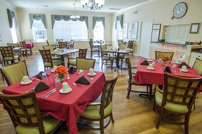A well-arranged dining room with tables set for a meal, featuring red tablecloths and wooden chairs.