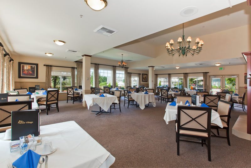 A spacious dining area with neatly arranged tables and chairs, featuring a chandelier and large windows.