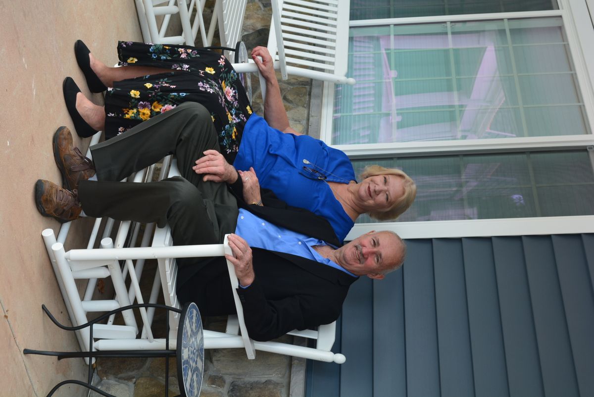 A couple sitting together on rocking chairs on a porch.