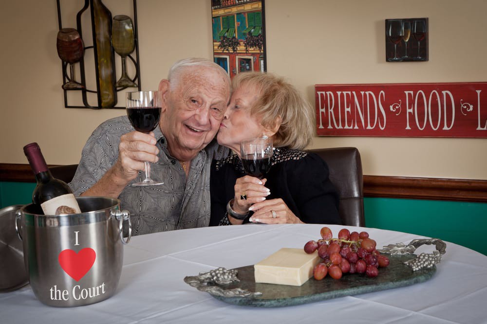 An elderly couple enjoying a glass of wine and sharing a sweet moment together.