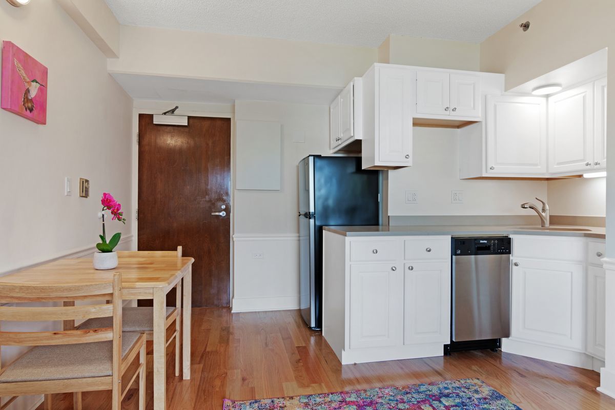 A modern apartment kitchen with white cabinets and hardwood flooring.