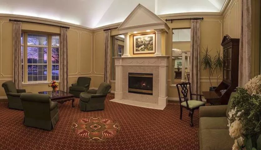 A cozy living room with a central fireplace, surrounded by comfortable armchairs and a patterned carpet.