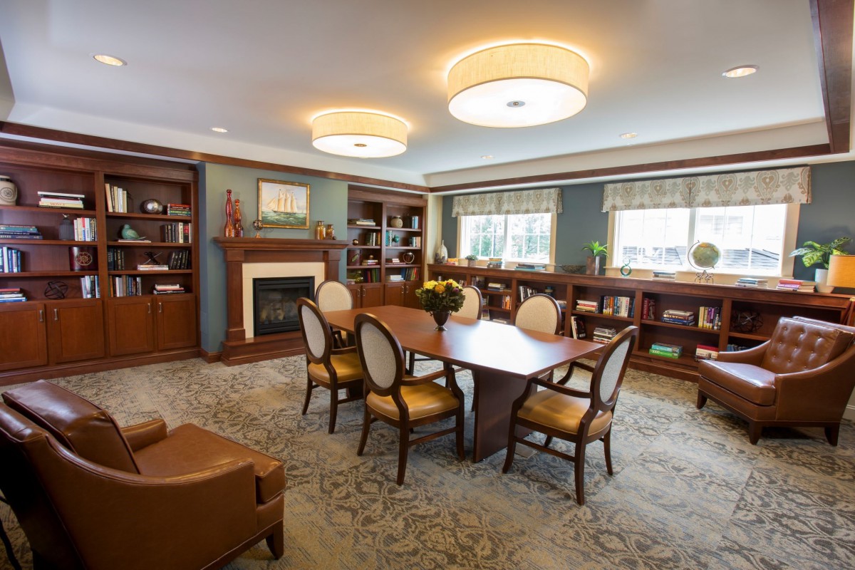A cozy living room featuring a wooden table surrounded by elegant chairs, built-in bookshelves, and a fireplace beneath soft lighting.